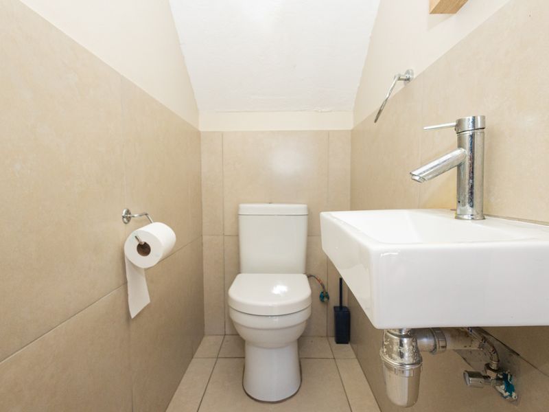 A compact guest bathroom featuring a modern wall-mounted basin with chrome tapware and a standard toilet, finished with neutral wall and floor tiling.