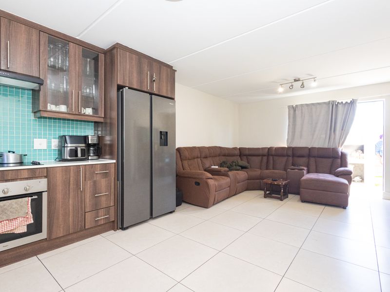 Open-plan living area featuring a modern kitchen with wood-finish cabinetry, tiled backsplash, and integrated appliances, flowing into a comfortable lounge space with tiled floors.
