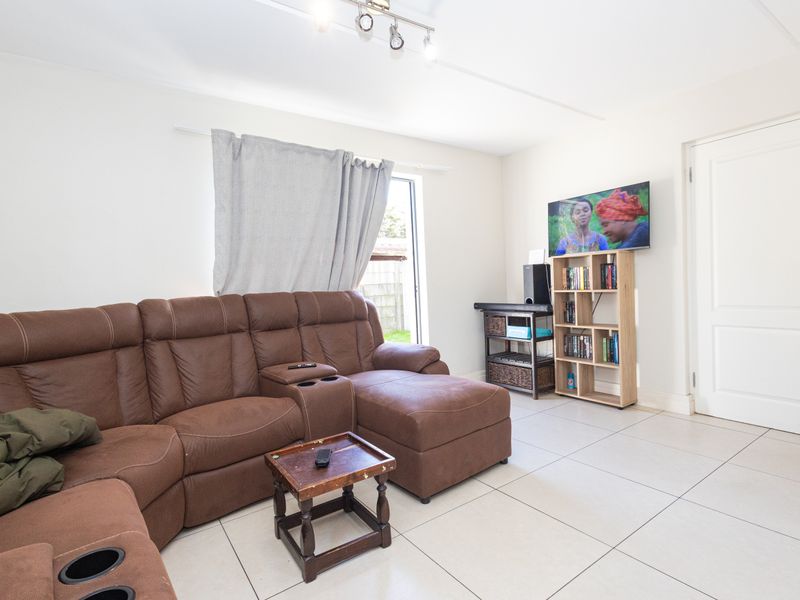 A bright living room featuring neutral tiled flooring, track lighting, and direct access to the outdoor area.