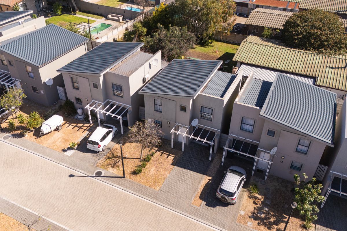 Aerial view of a townhouse complex featuring modern units with corrugated metal roofs, paved driveways, and attached pergolas.