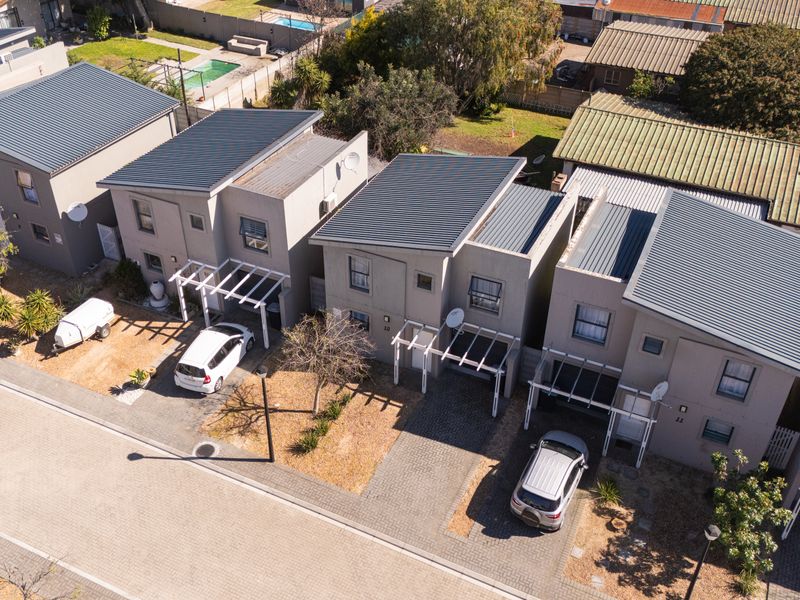 Aerial view of a townhouse complex featuring modern units with corrugated metal roofs, paved driveways, and attached pergolas.
