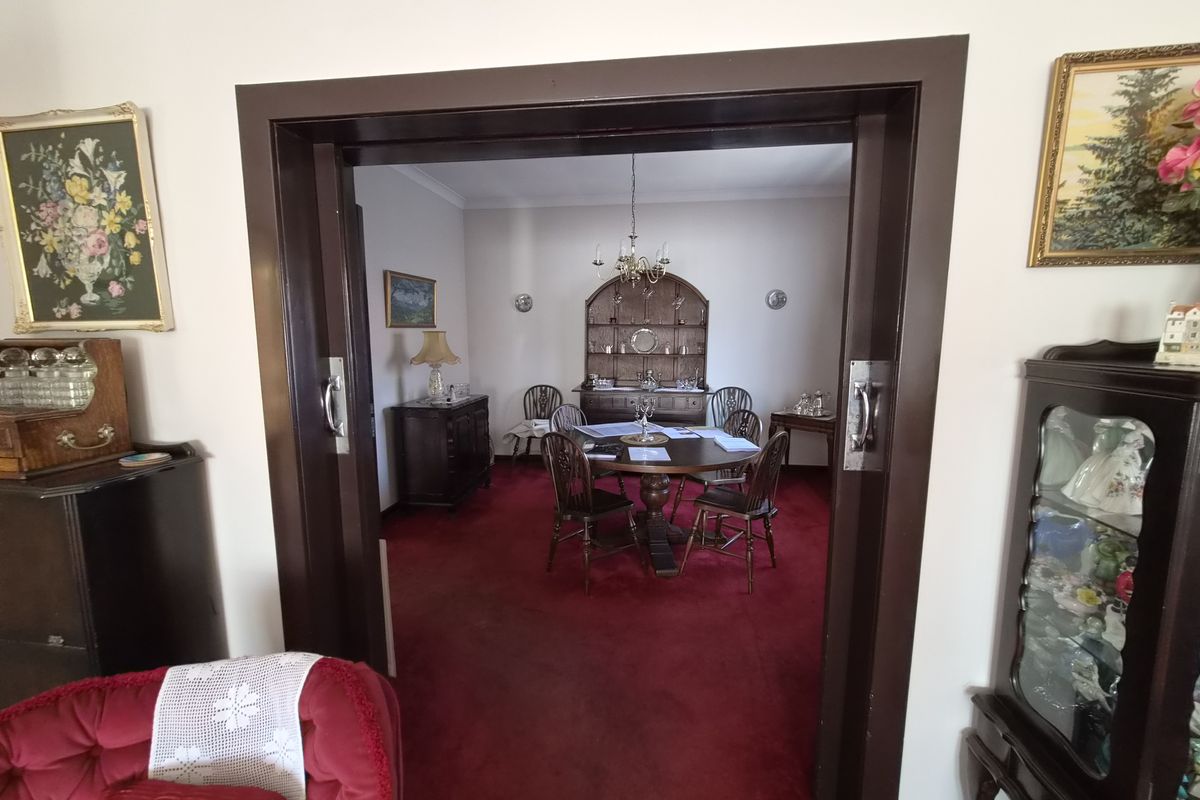 A formal dining room viewed through a dark wood sliding door, featuring a central chandelier, wall sconces, and red carpeting.