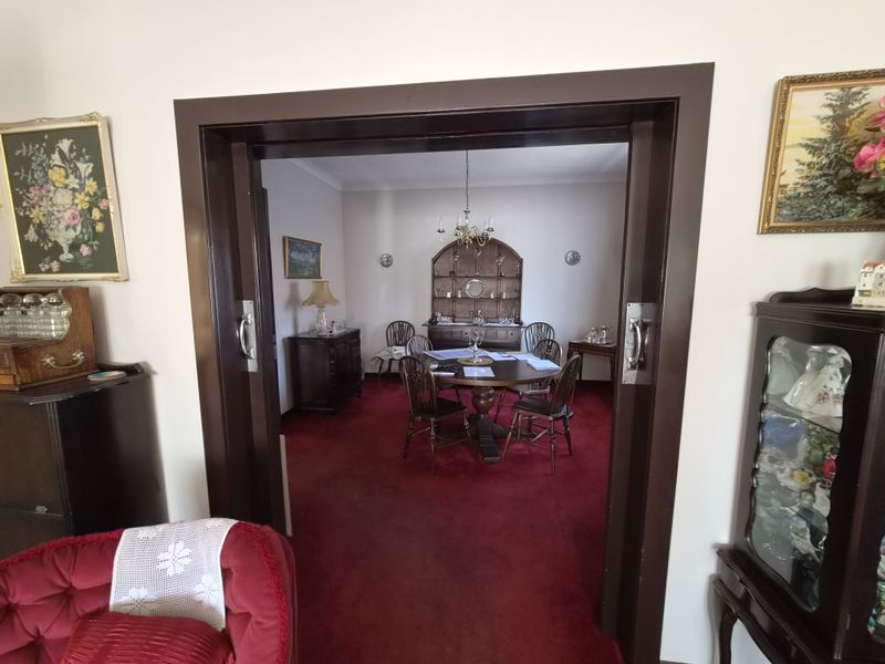 A formal dining room viewed through a dark wood sliding door, featuring a central chandelier, wall sconces, and red carpeting.