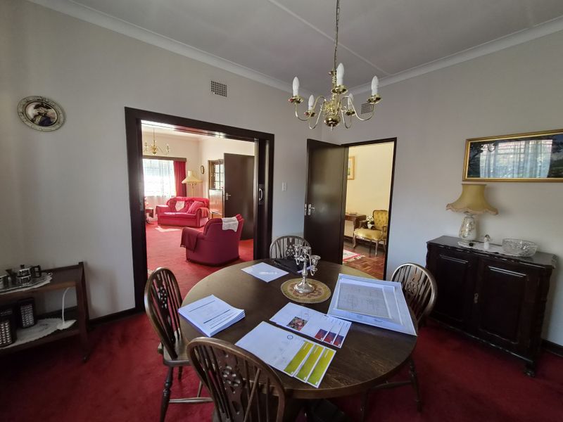 A traditional dining room featuring a central chandelier, coved cornicing, and timber door frames, providing access to adjacent living and hallway spaces.