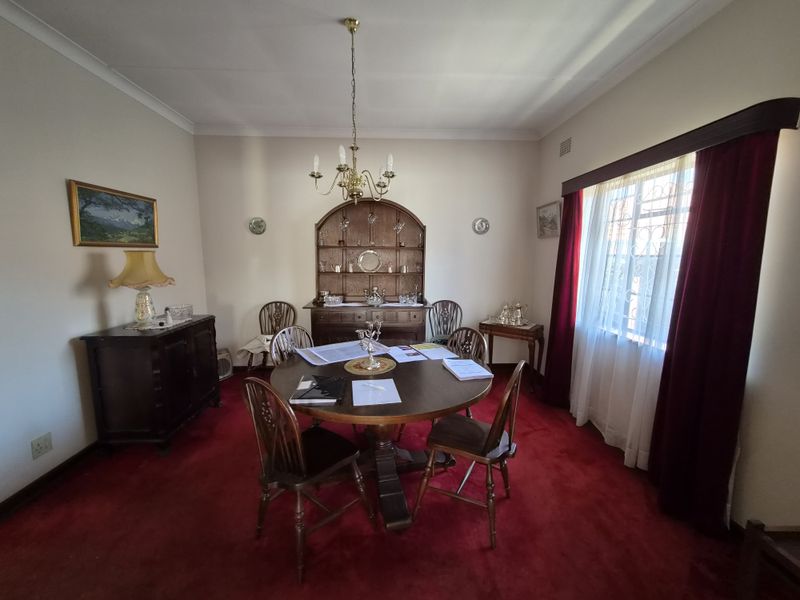A traditional dining room featuring coving, a central chandelier, and window security bars, finished with carpeted flooring.