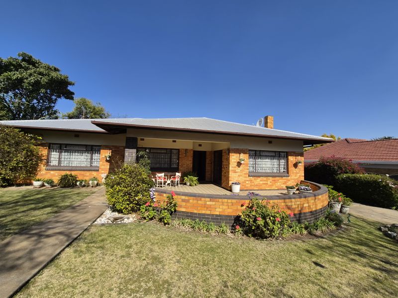 A well-maintained single-story brick house featuring a covered front patio, a curved brick retaining wall, and a neat front garden.