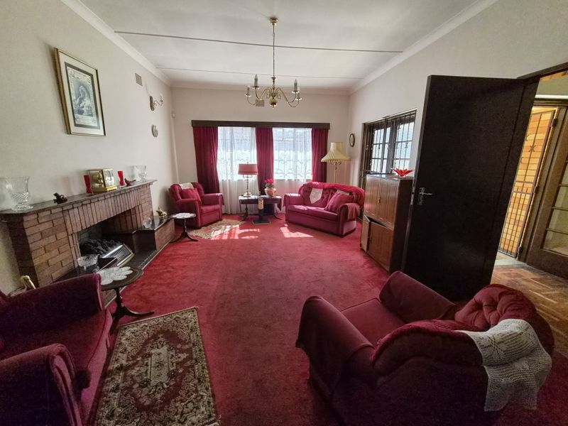 Spacious living room featuring a traditional brick fireplace, classic chandelier lighting, and large windows allowing for natural light.
