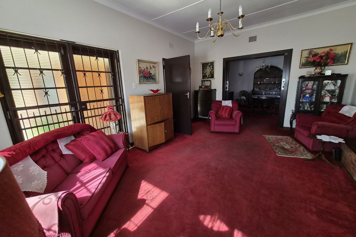 Spacious living room featuring red carpeting, a classic chandelier, and sliding doors with security gates leading to the exterior.