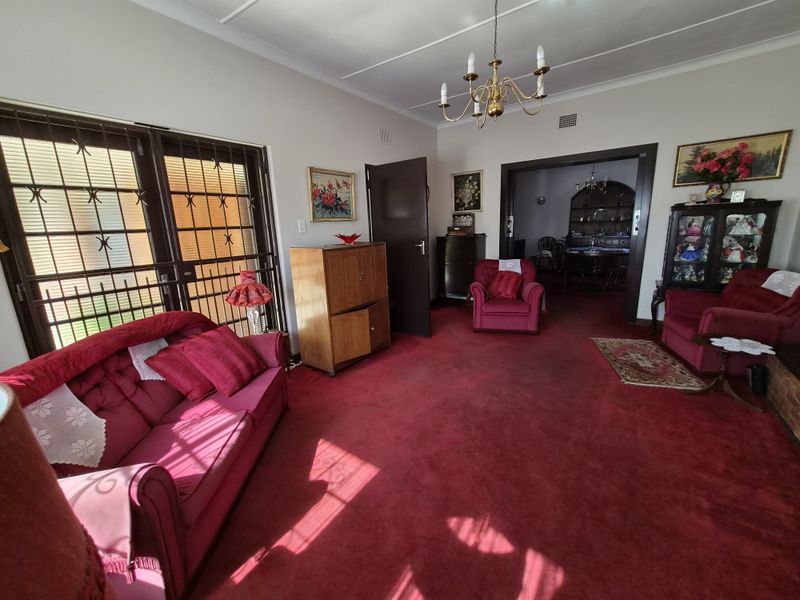 Spacious living room featuring red carpeting, a classic chandelier, and sliding doors with security gates leading to the exterior.