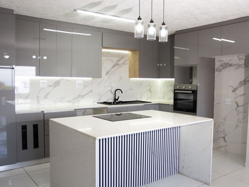 Modern kitchen featuring high-gloss grey cabinetry, marble-look splashbacks, a central island with an induction hob, and integrated built-in oven.