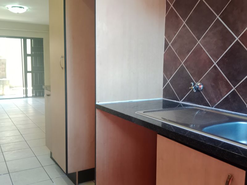 A functional kitchen area featuring built-in cabinetry, a stainless steel sink, and dark tiled backsplash, leading into an open-plan living space.