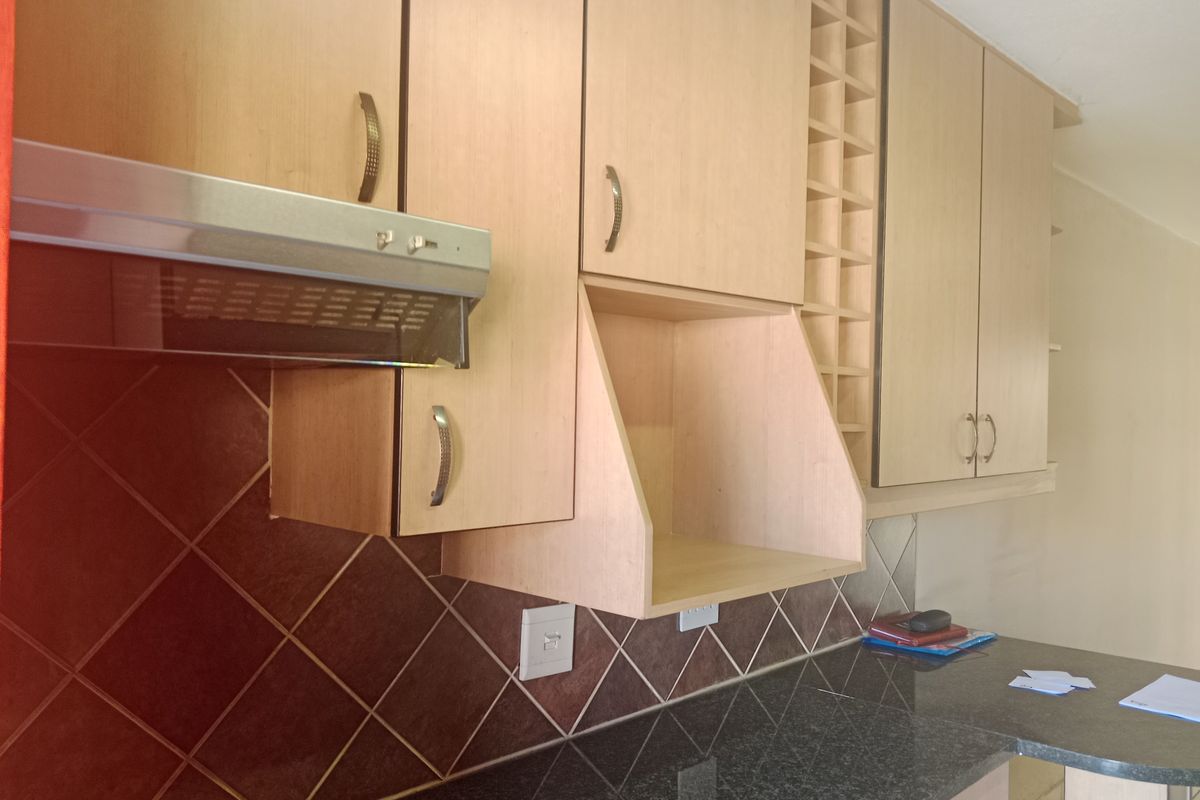 A functional kitchen area featuring light wood-finish cabinetry, a dark granite countertop, a built-in extractor fan, and a decorative wine rack.