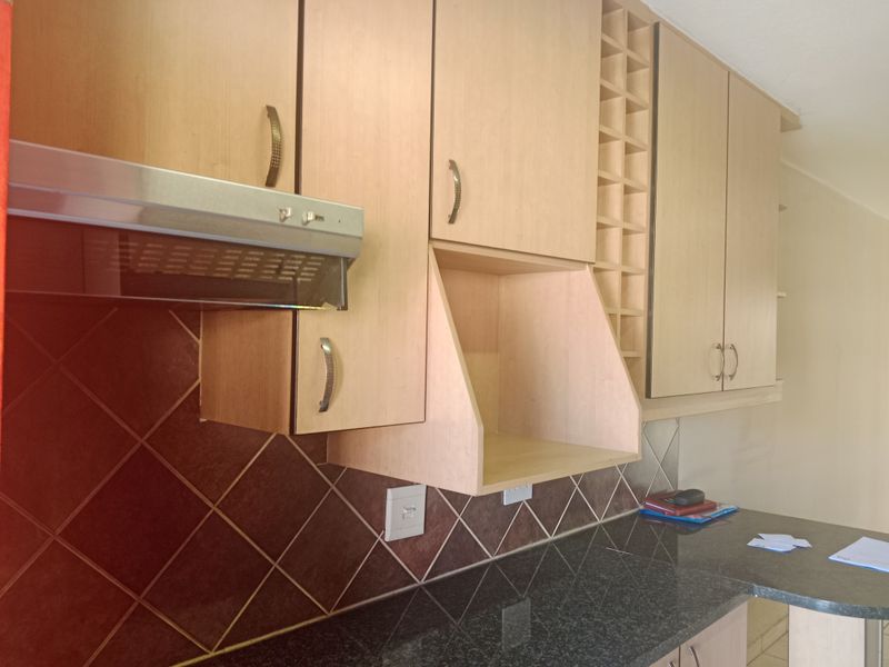 A functional kitchen area featuring light wood-finish cabinetry, a dark granite countertop, a built-in extractor fan, and a decorative wine rack.