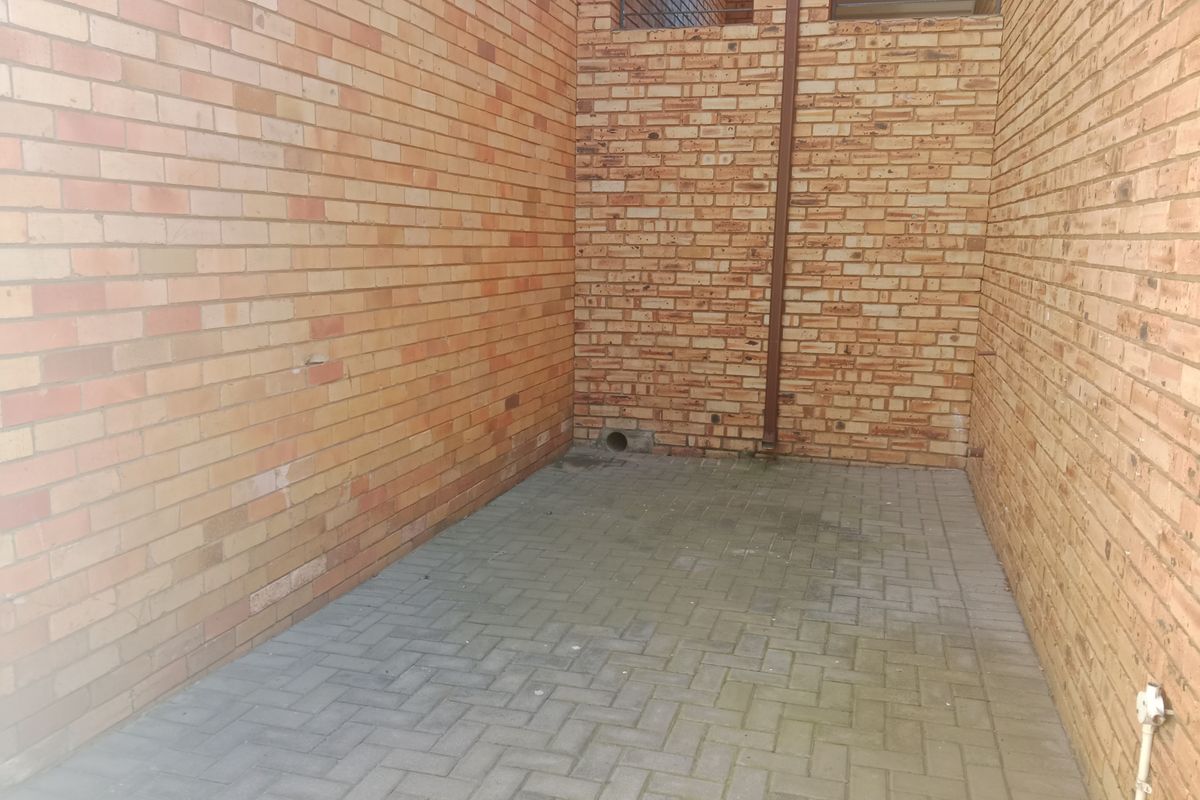 A private, paved rear courtyard area enclosed by face brick walls, featuring a functional downpipe and basic utility space.