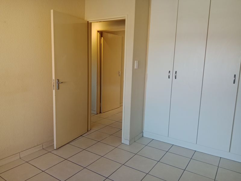An empty bedroom featuring tiled flooring and built-in cupboards, with a view into the adjacent hallway.