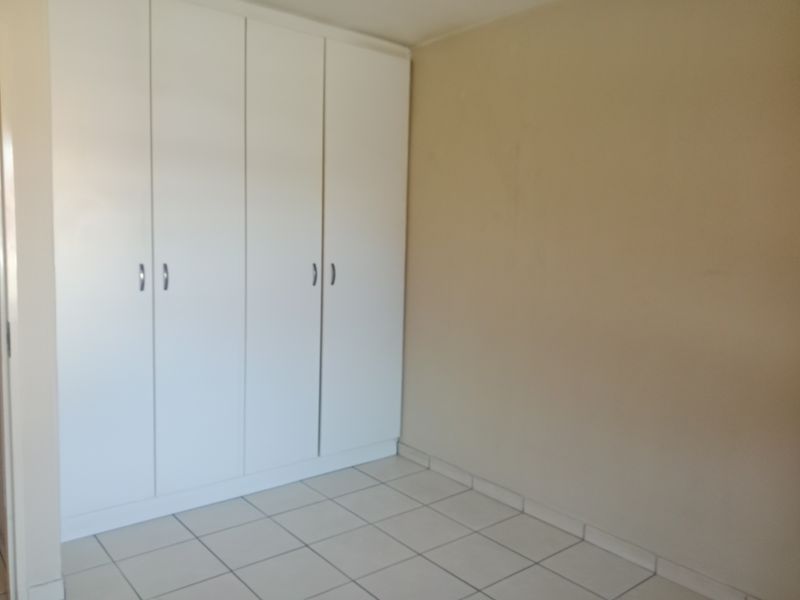A clean, empty bedroom featuring neutral wall paint, white built-in cupboards, and tiled flooring.