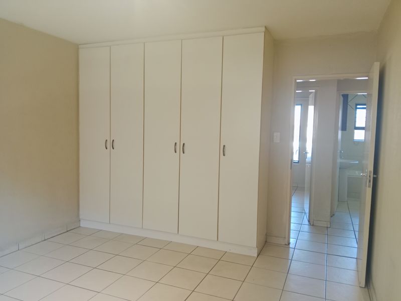 A spacious bedroom featuring neutral tiled flooring and extensive built-in cupboard storage, with direct access to an adjoining bathroom.