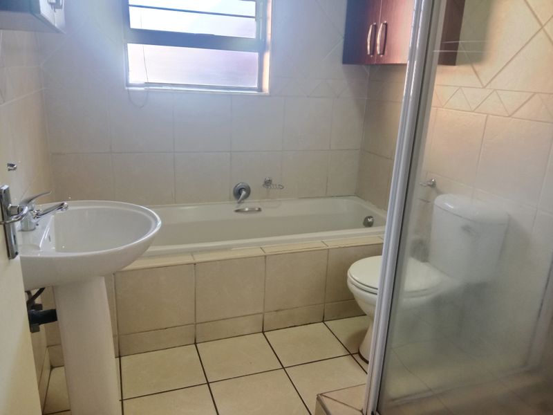 A functional bathroom featuring a pedestal basin, built-in bathtub, toilet, and a separate shower enclosure with tiled finishes throughout.