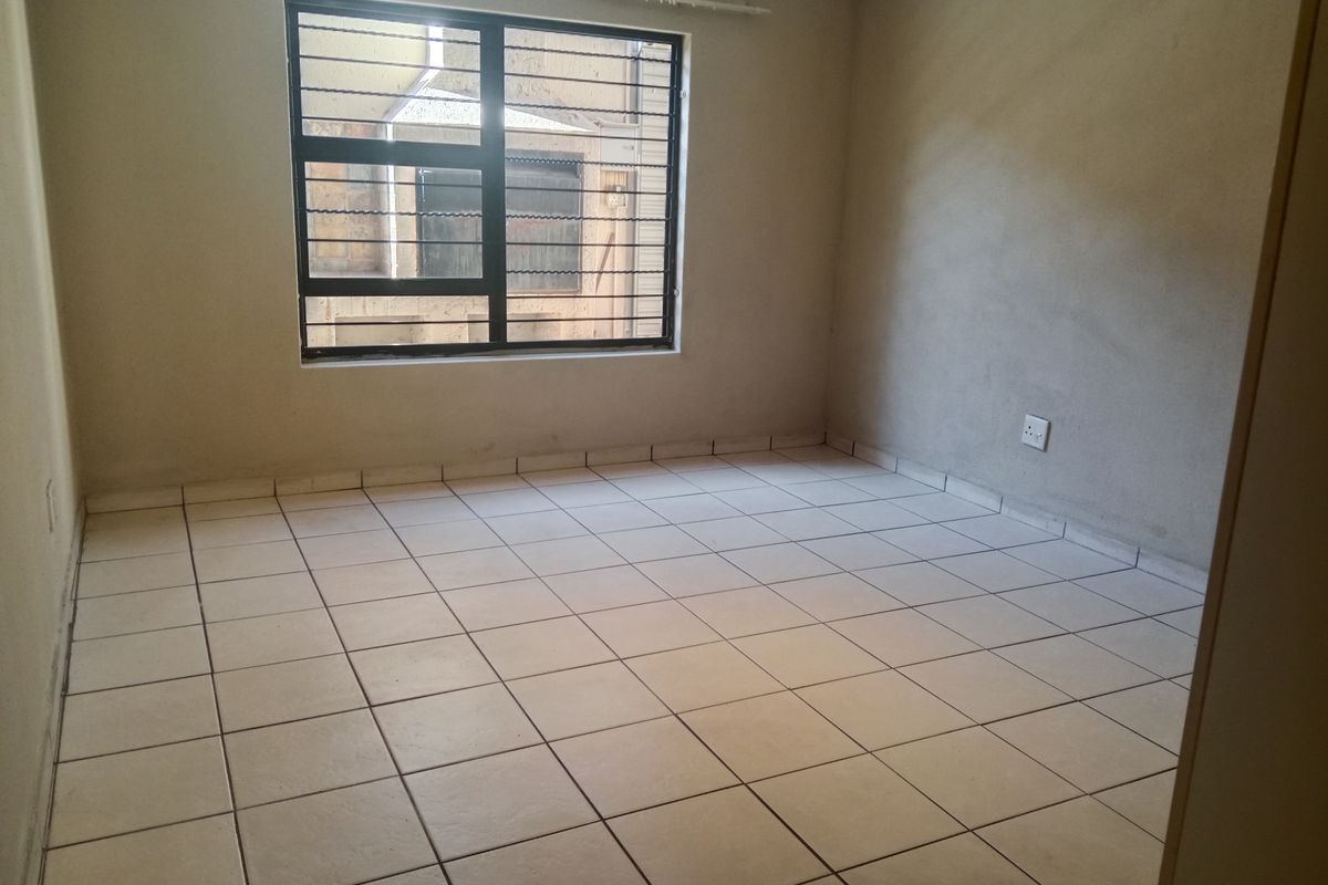 An empty bedroom featuring tiled flooring and a window with security bars, requiring finishing touches to the wall surfaces.