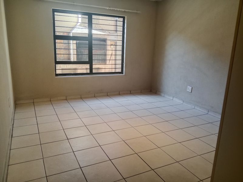 An empty bedroom featuring tiled flooring and a window with security bars, requiring finishing touches to the wall surfaces.
