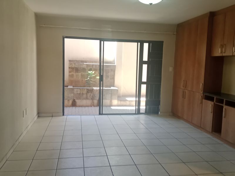 An empty open-plan living area featuring tiled floors, built-in wooden cabinetry, and a sliding glass door leading to a private courtyard with a stone feature.