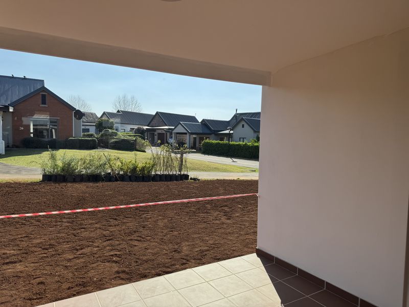 A covered patio area overlooking a freshly prepared garden space with surrounding residential properties in view.