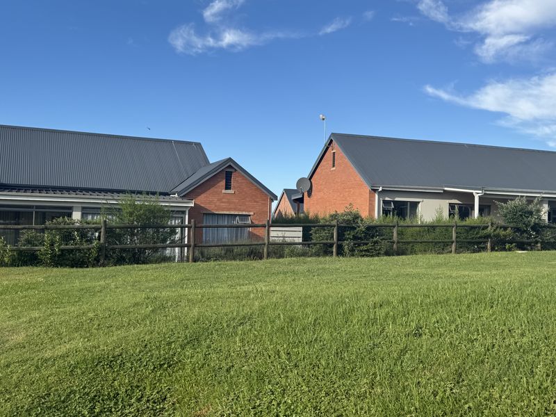 Rear view of the townhouse complex featuring brick facades, corrugated metal roofing, and a shared lawn area enclosed by a timber fence.