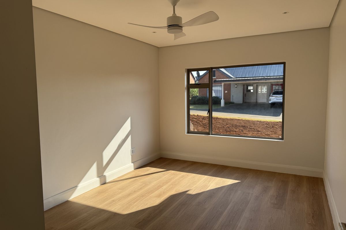 A bright, empty bedroom featuring modern laminate flooring, a ceiling fan, recessed lighting, and a large window with views of the exterior.