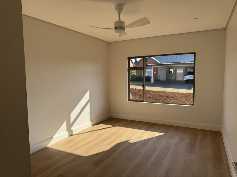 A bright, empty bedroom featuring modern laminate flooring, a ceiling fan, recessed lighting, and a large window with views of the exterior.