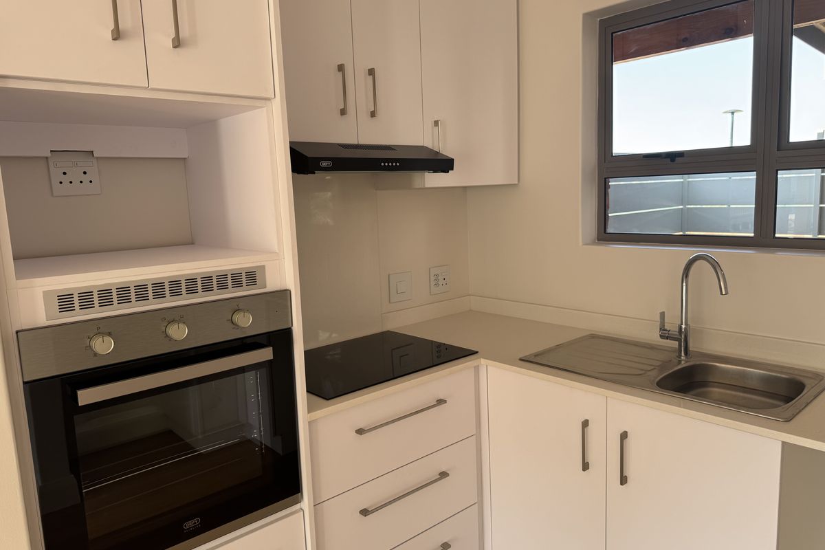A clean, modern kitchen featuring white cabinetry, stone countertops, a built-in oven, electric hob, extractor fan, and a stainless steel sink.