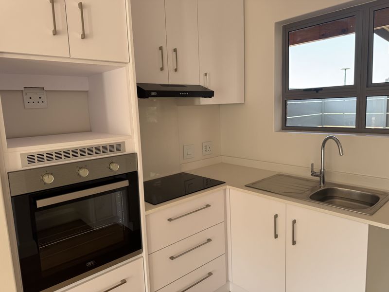 A clean, modern kitchen featuring white cabinetry, stone countertops, a built-in oven, electric hob, extractor fan, and a stainless steel sink.