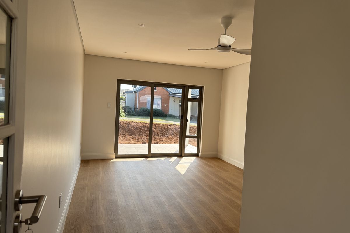 A bright, empty living room featuring modern laminate flooring, a ceiling fan, and large sliding glass doors providing access to the exterior.