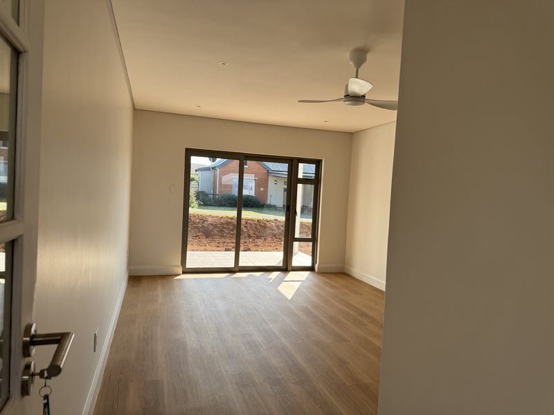 A bright, empty living room featuring modern laminate flooring, a ceiling fan, and large sliding glass doors providing access to the exterior.