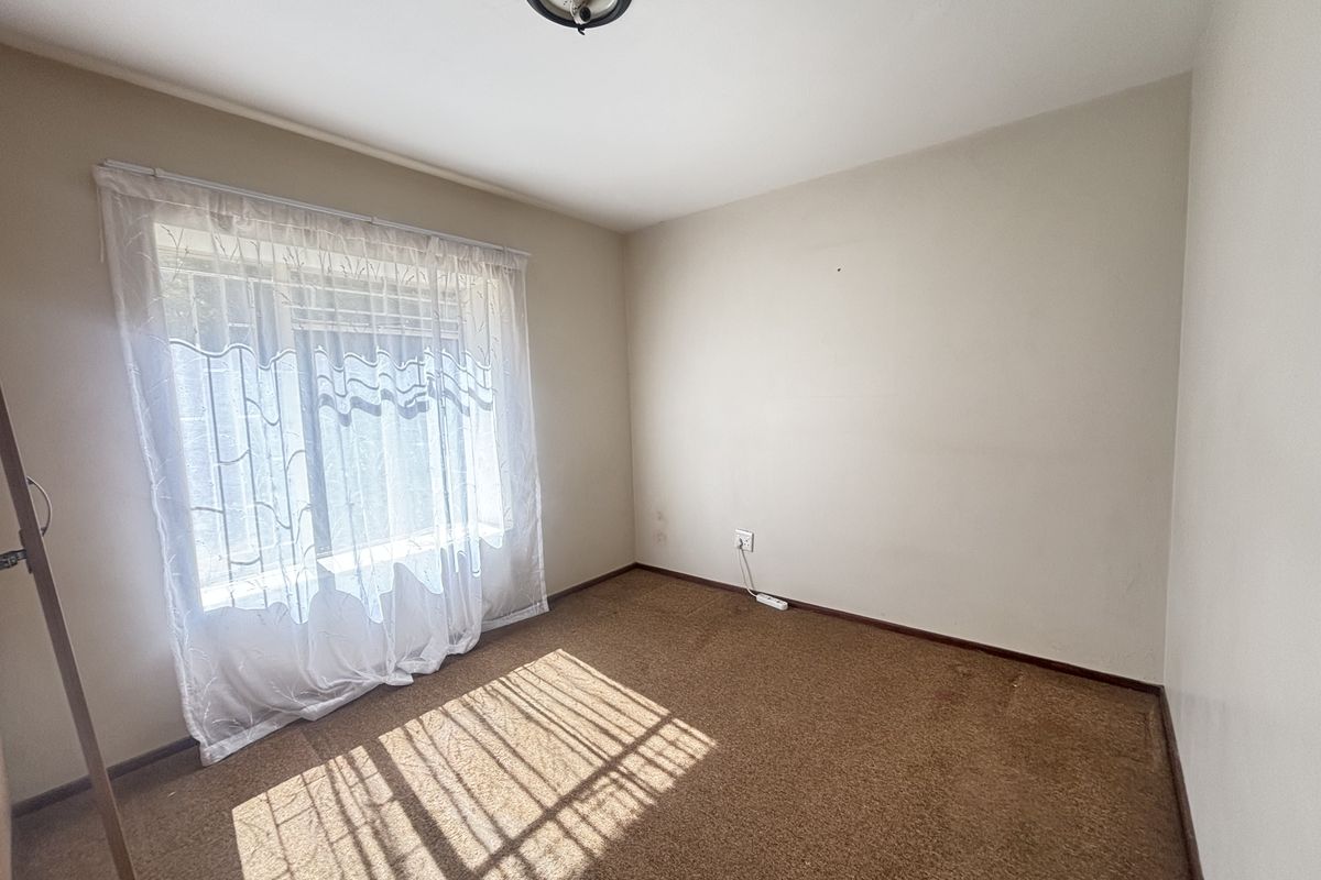 A vacant bedroom featuring carpeted flooring, a window with curtains, and a central ceiling light fixture, offering a blank canvas for personalization.