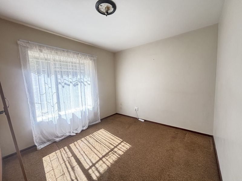 A vacant bedroom featuring carpeted flooring, a window with curtains, and a central ceiling light fixture, offering a blank canvas for personalization.
