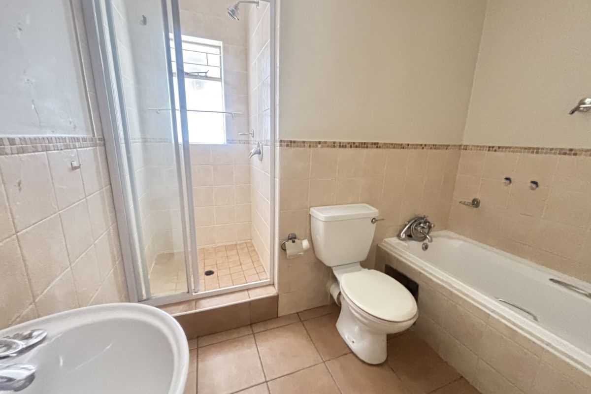A functional bathroom featuring a separate shower enclosure, built-in bathtub, toilet, and pedestal basin with neutral wall and floor tiling.