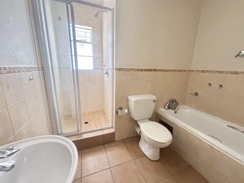 A functional bathroom featuring a separate shower enclosure, built-in bathtub, toilet, and pedestal basin with neutral wall and floor tiling.