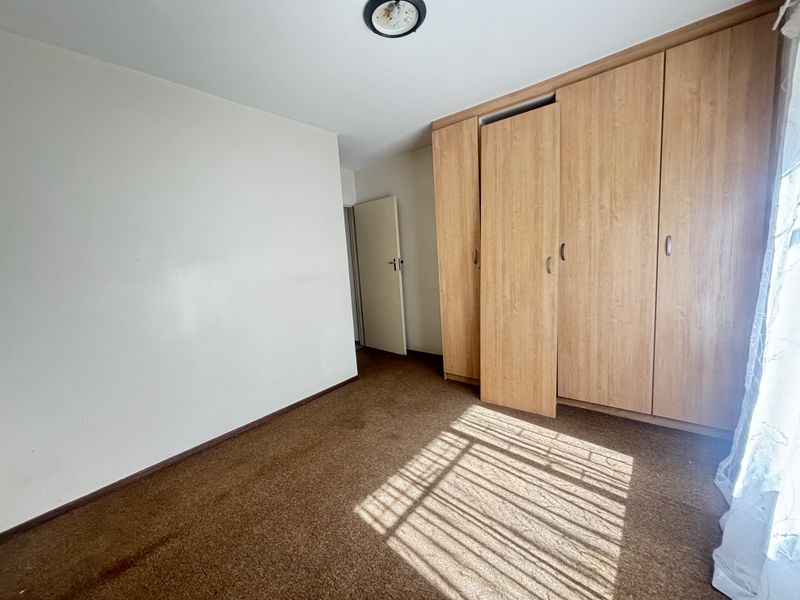 A vacant bedroom featuring built-in wooden cupboards and carpeted flooring, offering a blank canvas for potential updates.