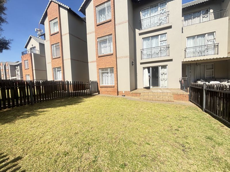 Rear view of a multi-story apartment building featuring a private garden, tiled patio area, and sliding door access to the ground floor unit.