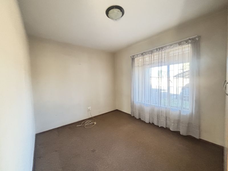 An empty bedroom featuring carpet flooring, a window with security bars, and a central ceiling light fixture.