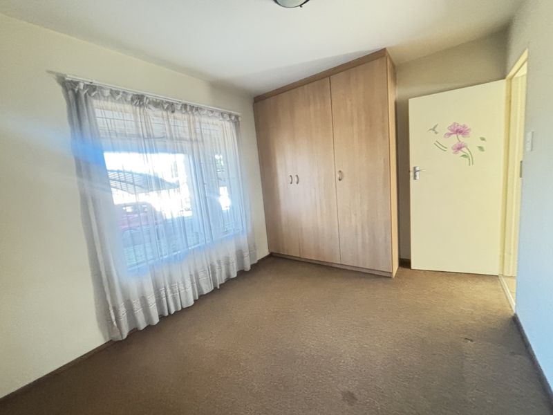 A vacant bedroom featuring neutral walls, carpeted flooring, and a built-in wooden wardrobe, offering a blank canvas for personalization.