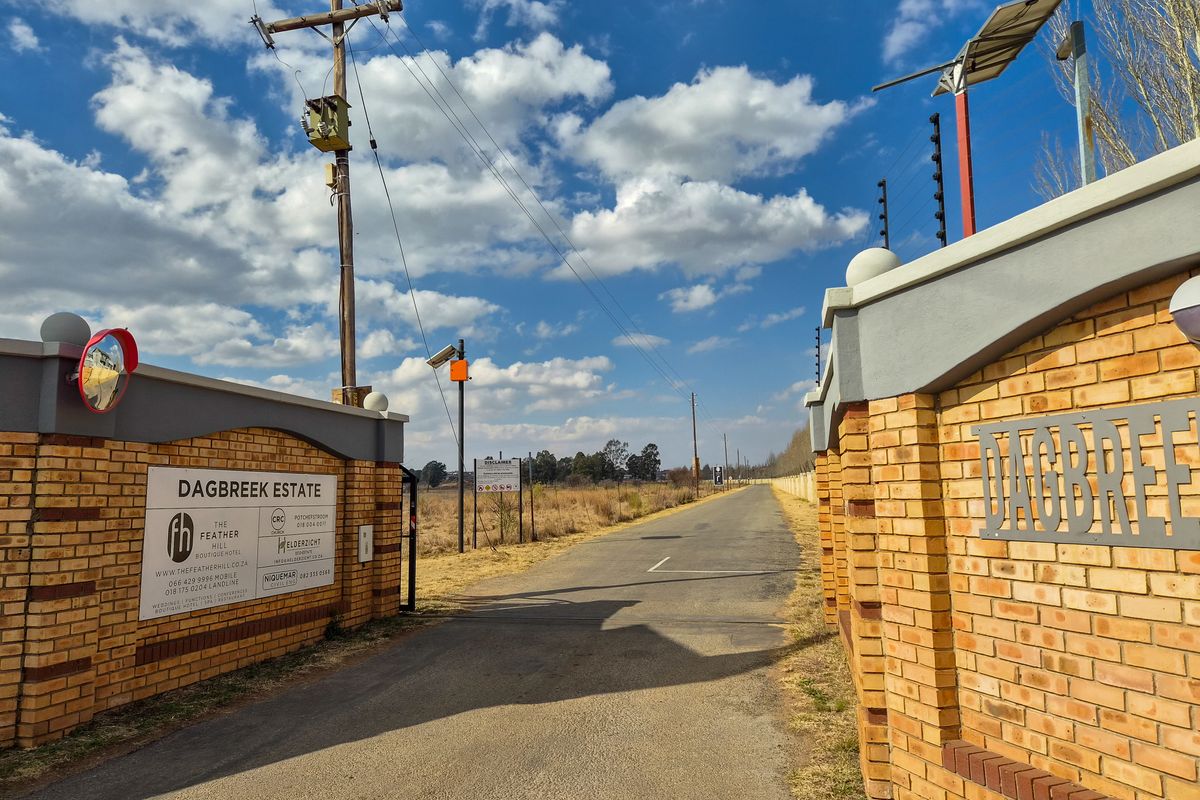 Entrance view of Dagbreek Estate featuring a brick boundary wall, electric fencing, and an asphalt driveway leading into the property.