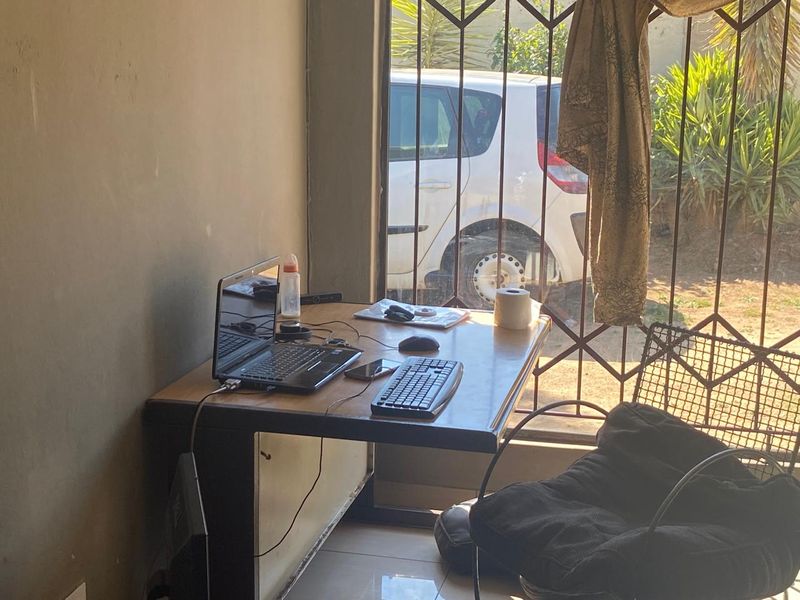 A small home office space featuring tiled flooring and a security gate, requiring cosmetic updates to improve the overall condition.