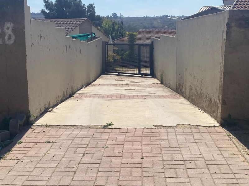 A private driveway entrance featuring paved surfaces, boundary walls, and a metal security gate, showing signs of wear and weathering.