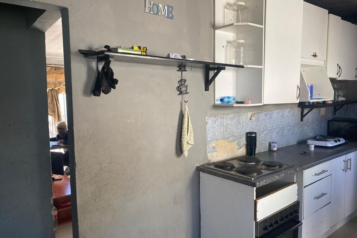 A functional kitchen area featuring built-in cabinetry, an electric hob, and oven, currently requiring cosmetic repairs to the wall plaster and cabinetry.