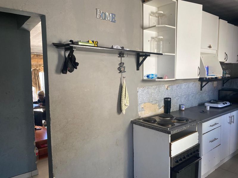 A functional kitchen area featuring built-in cabinetry, an electric hob, and oven, currently requiring cosmetic repairs to the wall plaster and cabinetry.