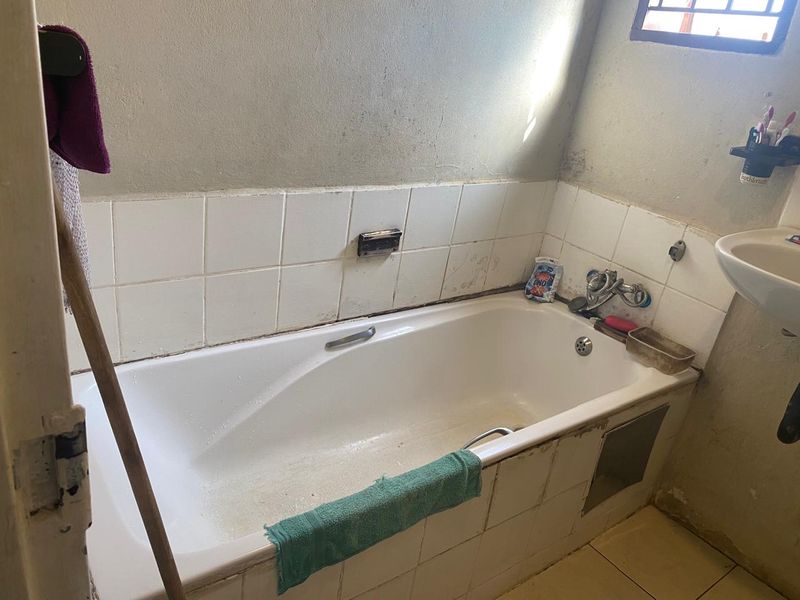 A dated bathroom featuring a standard bathtub with wall-mounted fixtures and a pedestal basin, requiring significant cosmetic updates and maintenance.