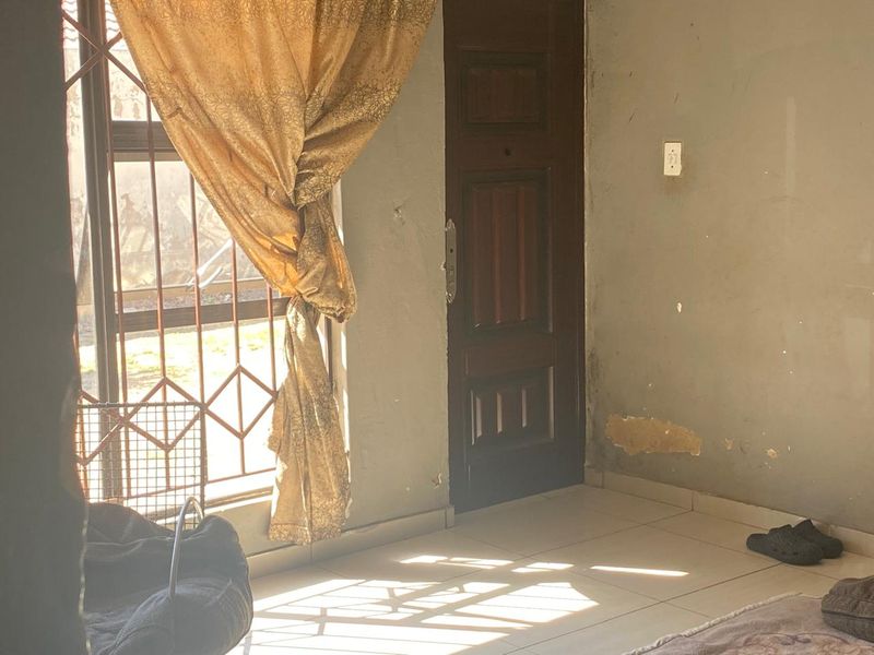An entry area featuring tiled flooring and a timber door, showing signs of wall surface damage and peeling paint requiring maintenance.