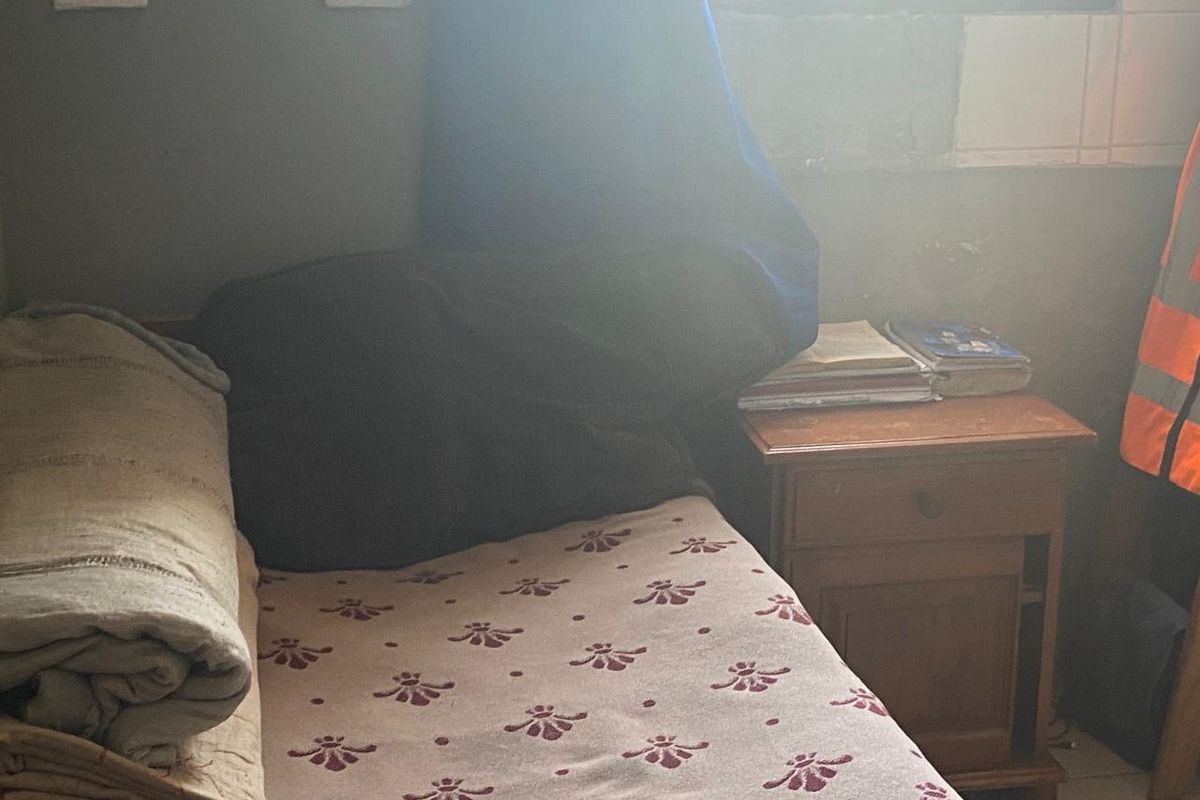A small bedroom featuring security bars on the window and basic electrical infrastructure, currently requiring cosmetic updates and wall finishing.