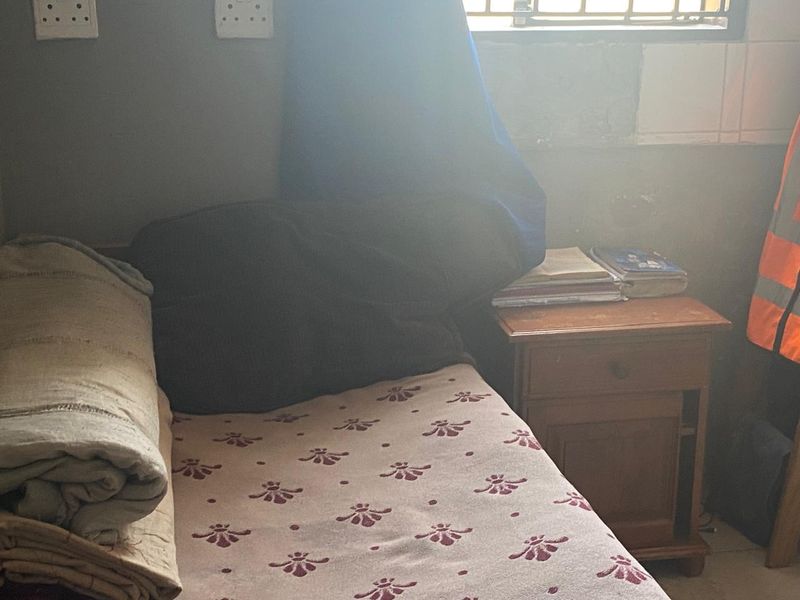 A small bedroom featuring security bars on the window and basic electrical infrastructure, currently requiring cosmetic updates and wall finishing.